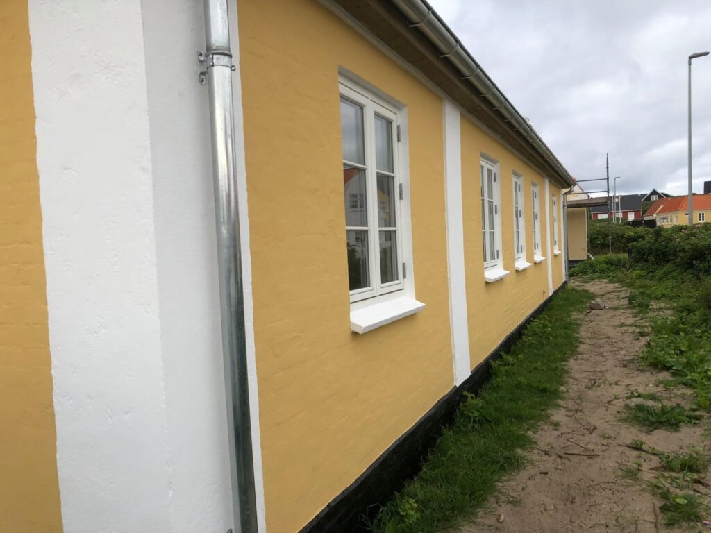 Gul murstenshus med hvide vinduer og græs langsiden.