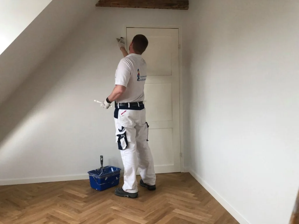 Malermester maler et værelse hvidt, set bagfra.