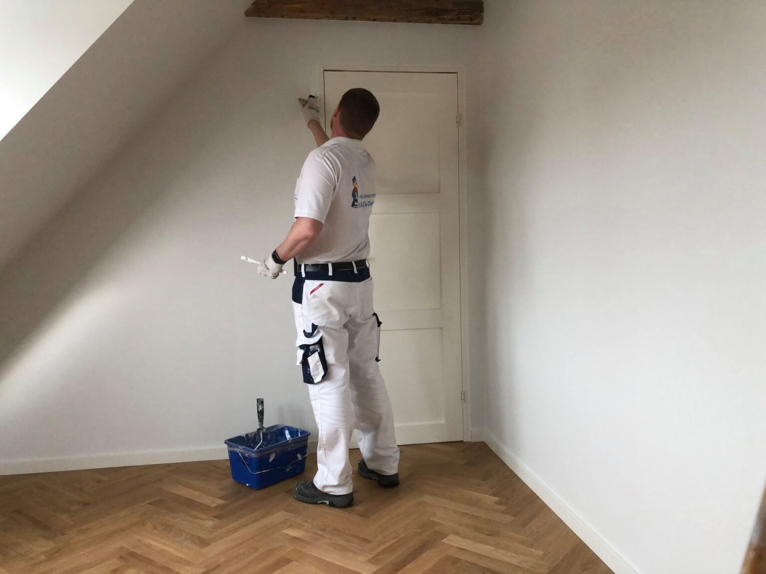 Malermester maler et værelse hvidt, set bagfra.